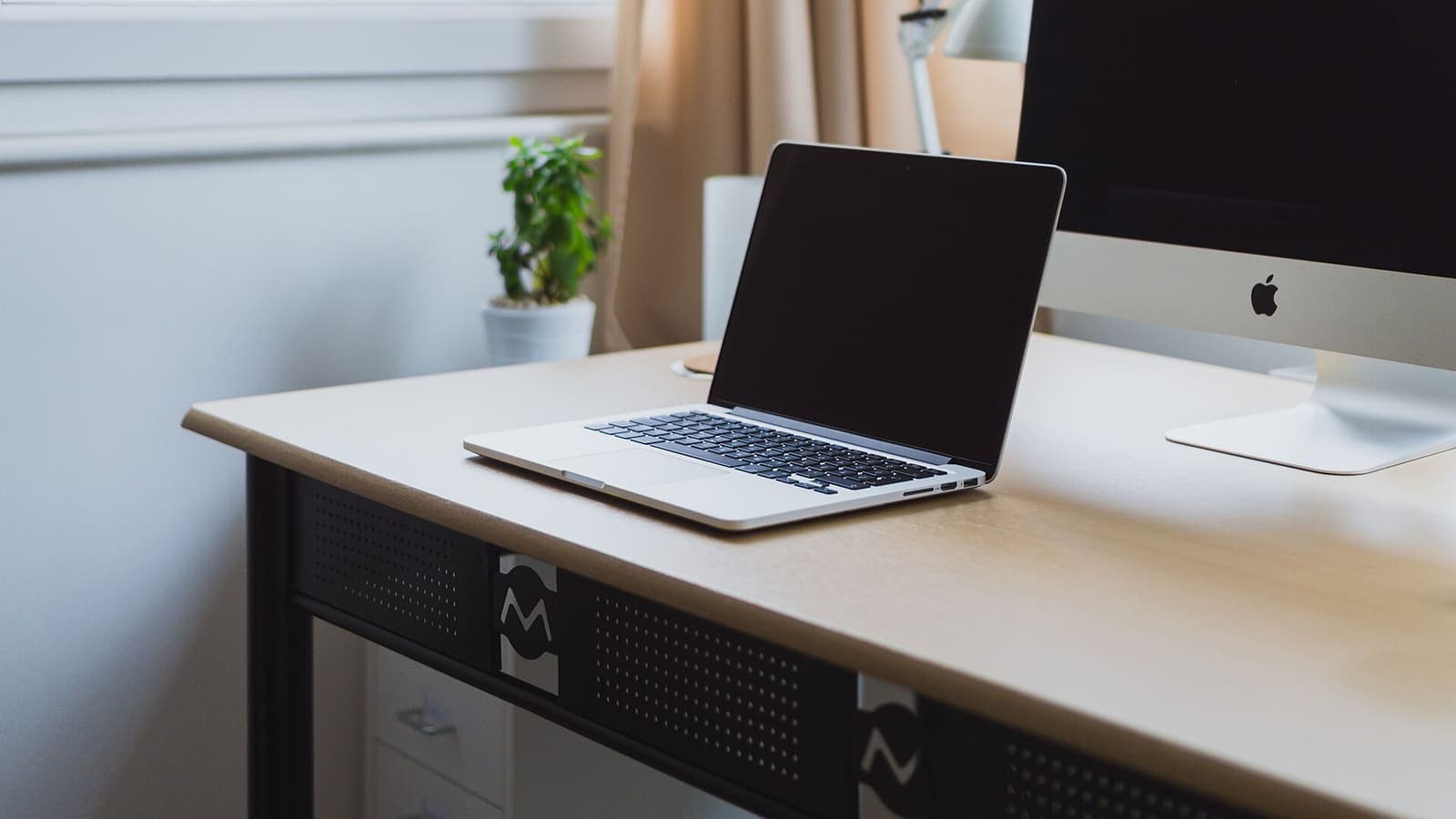 Opengeklapte laptop op een opgeruimd bureau naast een monitor